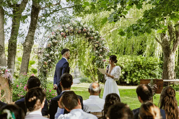 La cérémonie de mariage de Camille et Mathieu sous une arche fleurie dans le parc du Mas de Peyre.