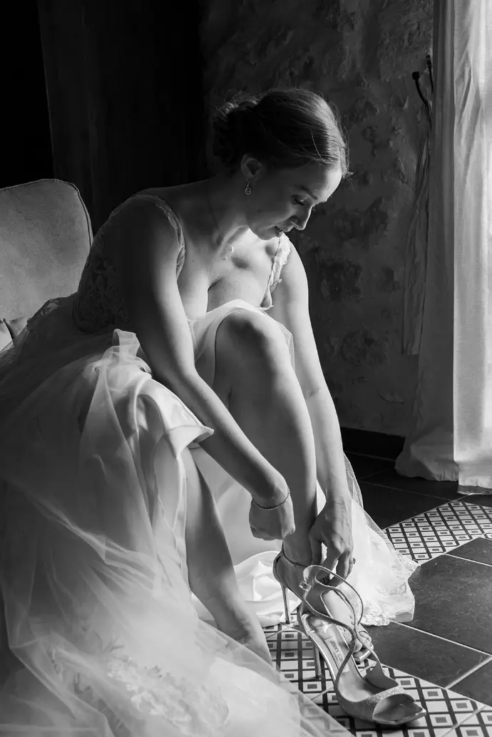 Estelle met sa chaussure dans un instant capturé en noir et blanc, juste avant la cérémonie de son mariage.