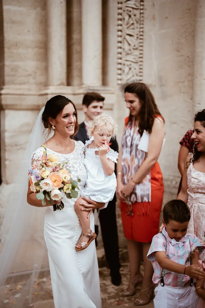 Sharlène porte sa fille à la sortie de l’église lors de leur mariage au Domaine du Grand Belly, un moment plein de tendresse.