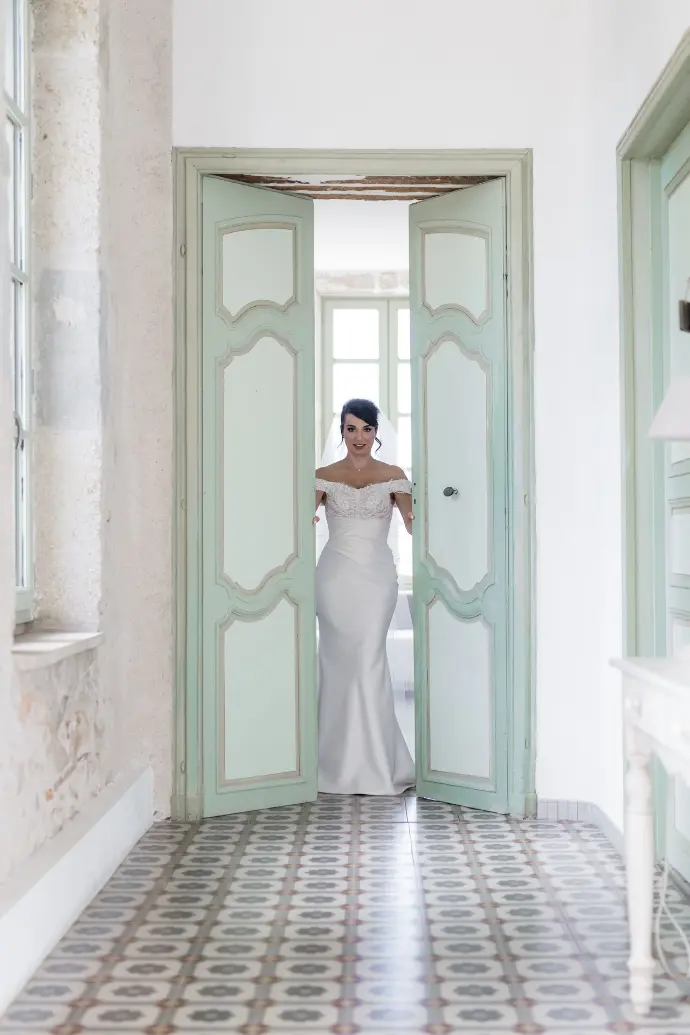 Mariée ouvrant une porte après ses préparatifs, moment de transition capté sur le vif, entre intimité et anticipation de la journée.
