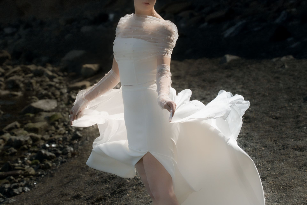 mariée en robe fluide marchant sur plage volcanique avec vent et mouvement